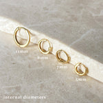 Set of gold hoop earrings with labeled internal diameters on a stone surface
