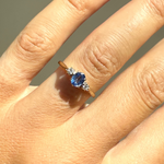Close-up of a hand wearing a ring with a blue gemstone on a neutral background