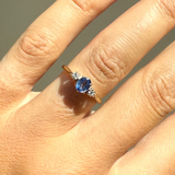 Close-up of a hand wearing a ring with a blue gemstone on a neutral background