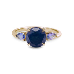 Gold ring with a blue gemstone and smaller purple stones on a white background