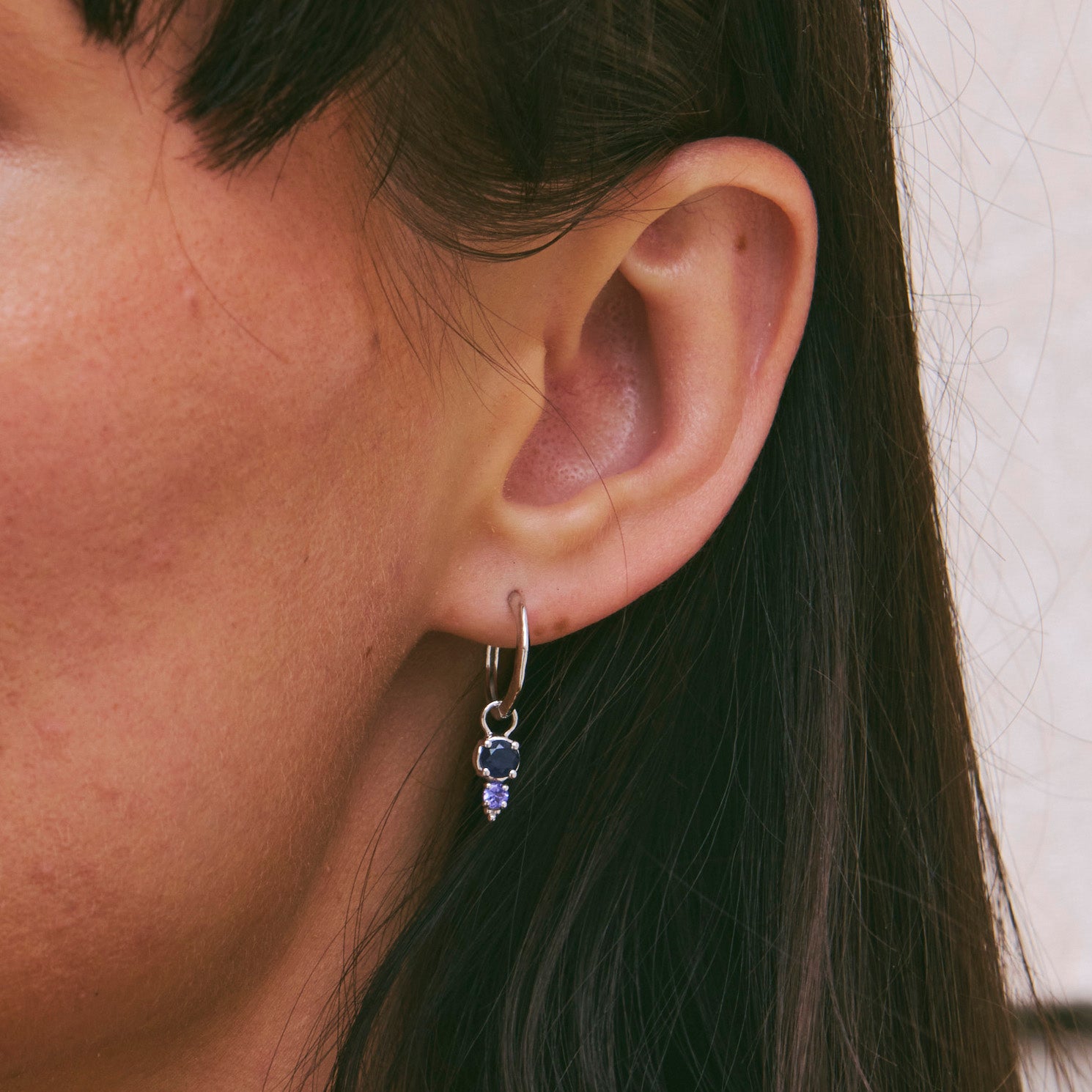 Close-up of an ear wearing a silver earring with purple gemstones.