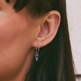 Close-up of an ear wearing a silver earring with purple gemstones.