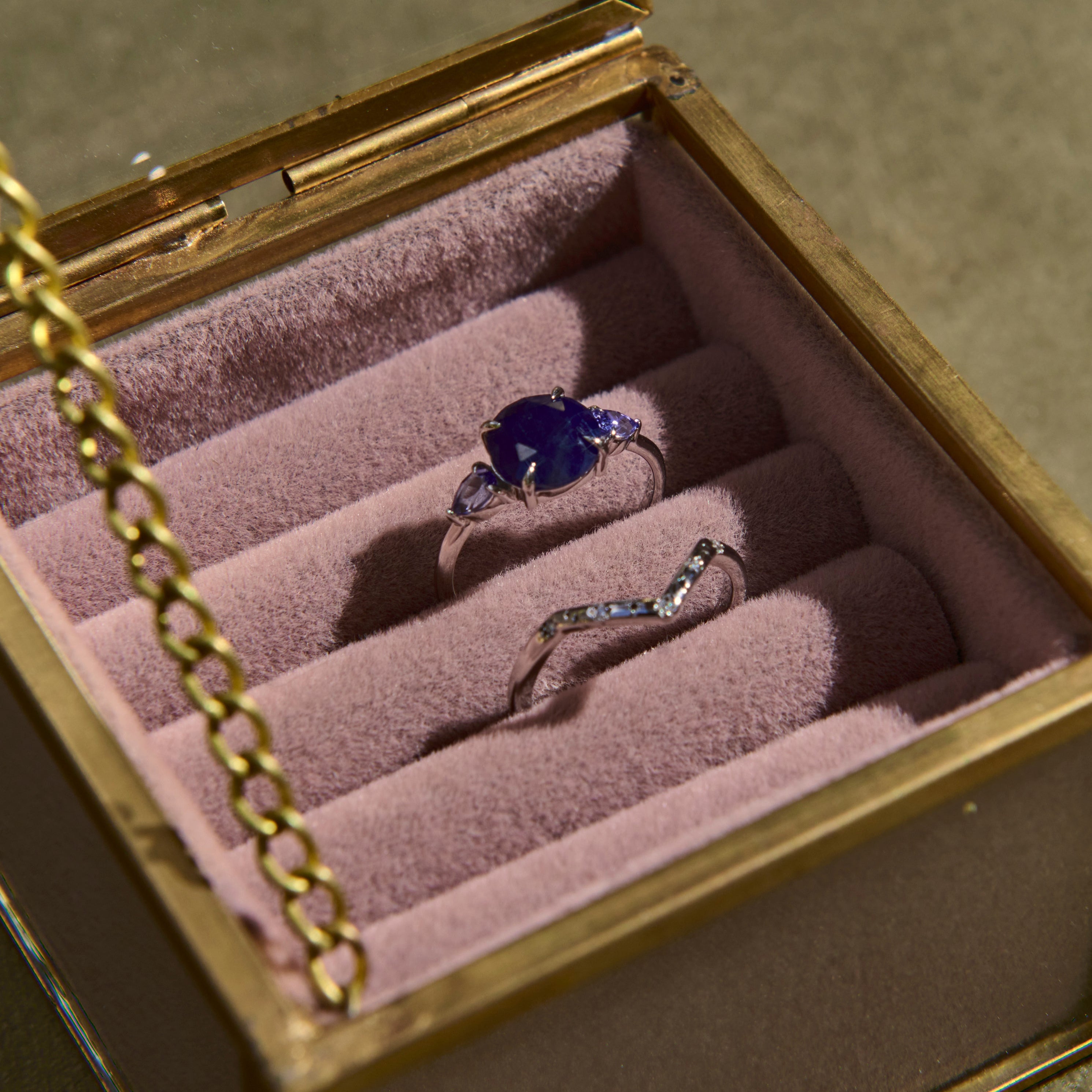 Two rings in a jewelry box with a gold chain on a green background