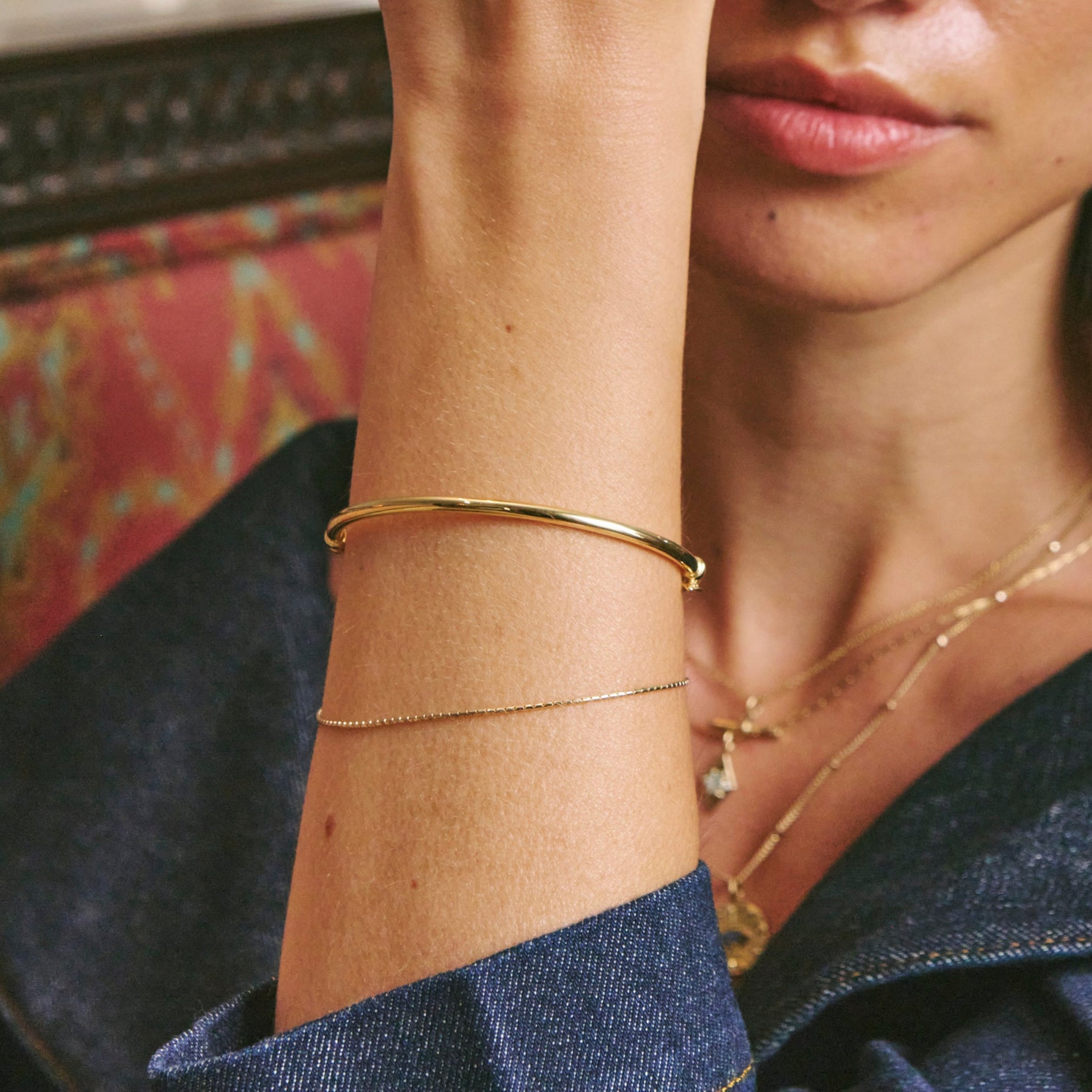 Close-up of a person wearing gold bracelets and a necklace with a colorful background.