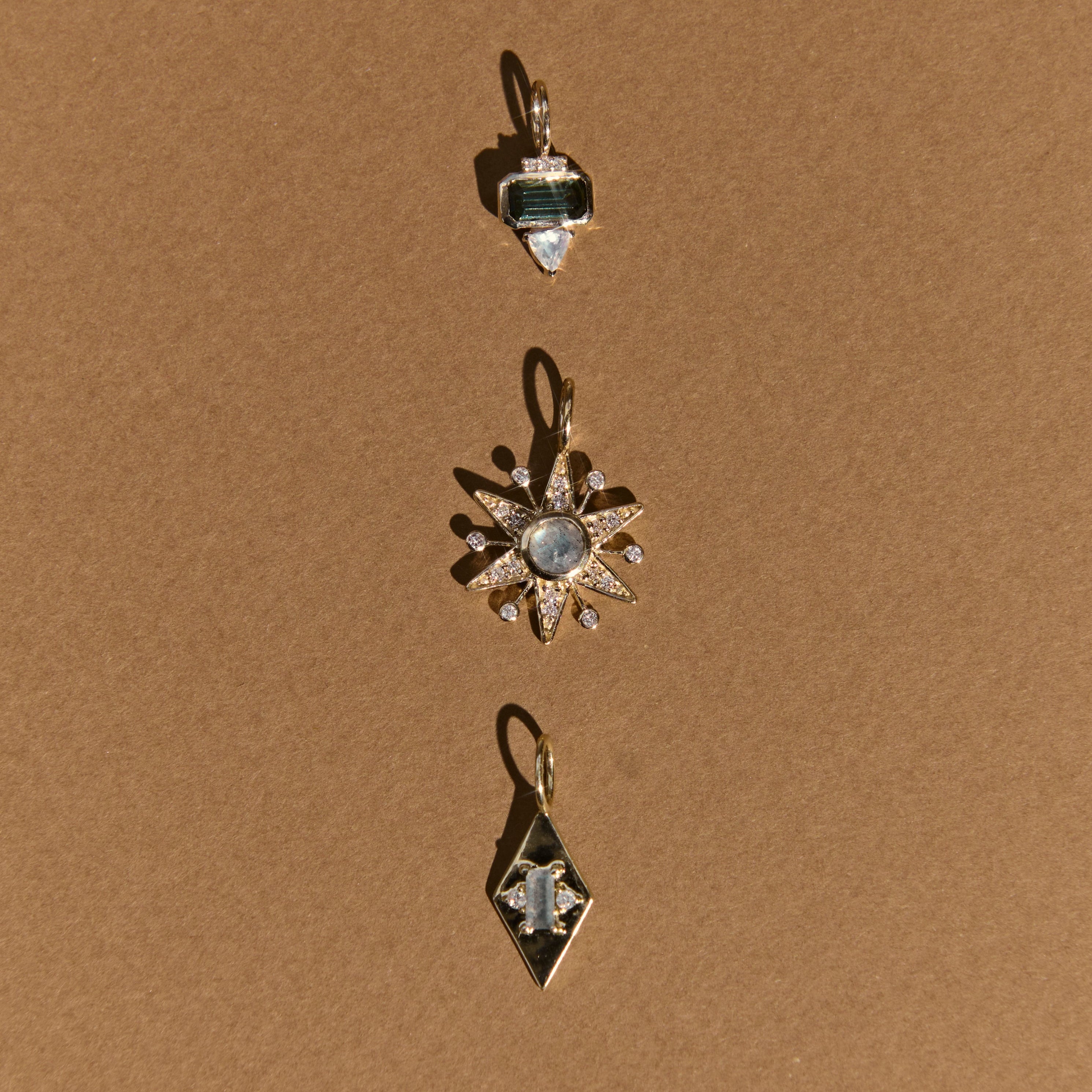 Three gold pendants with gemstones on a brown background
