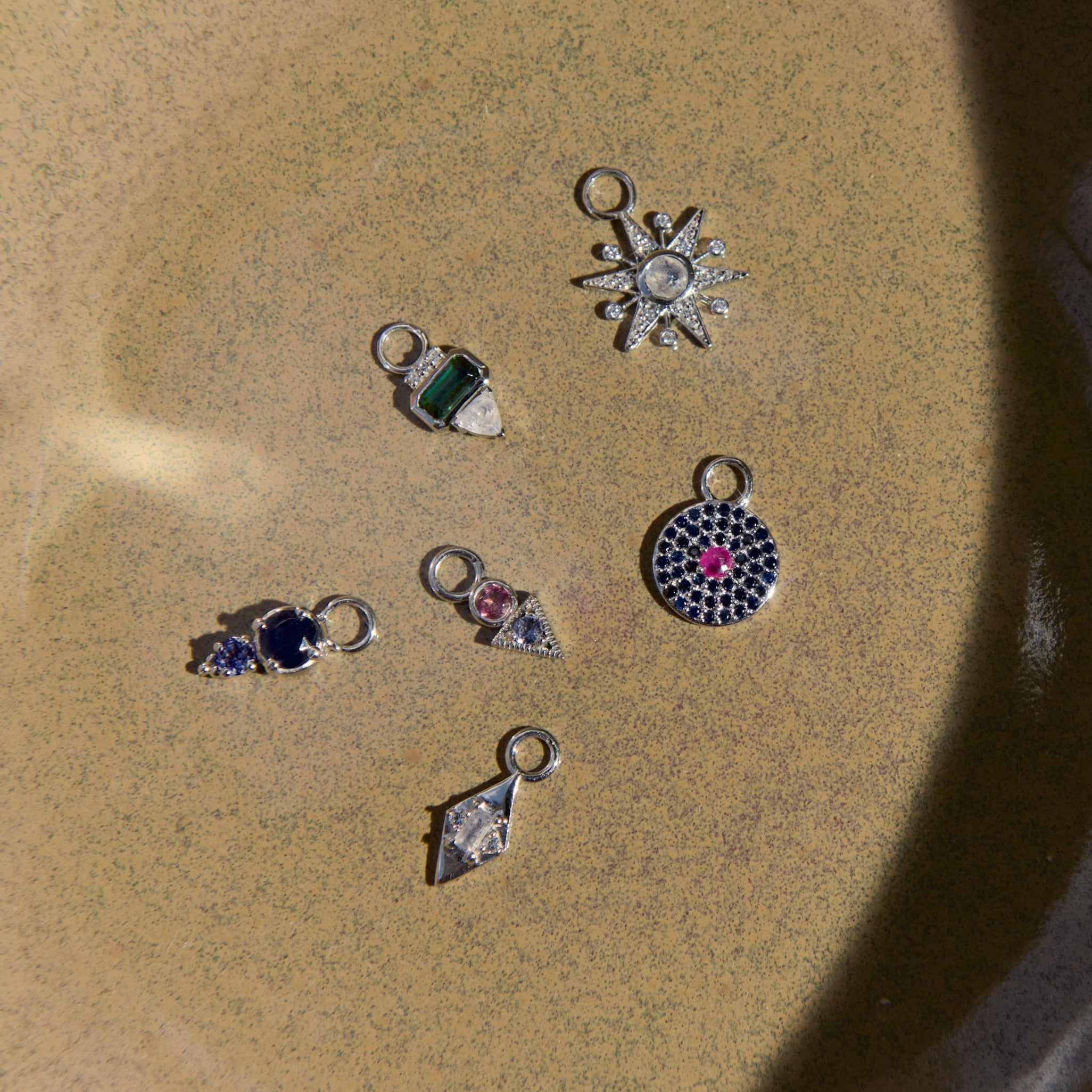 Collection of silver earring charms with gemstones on a textured beige surface