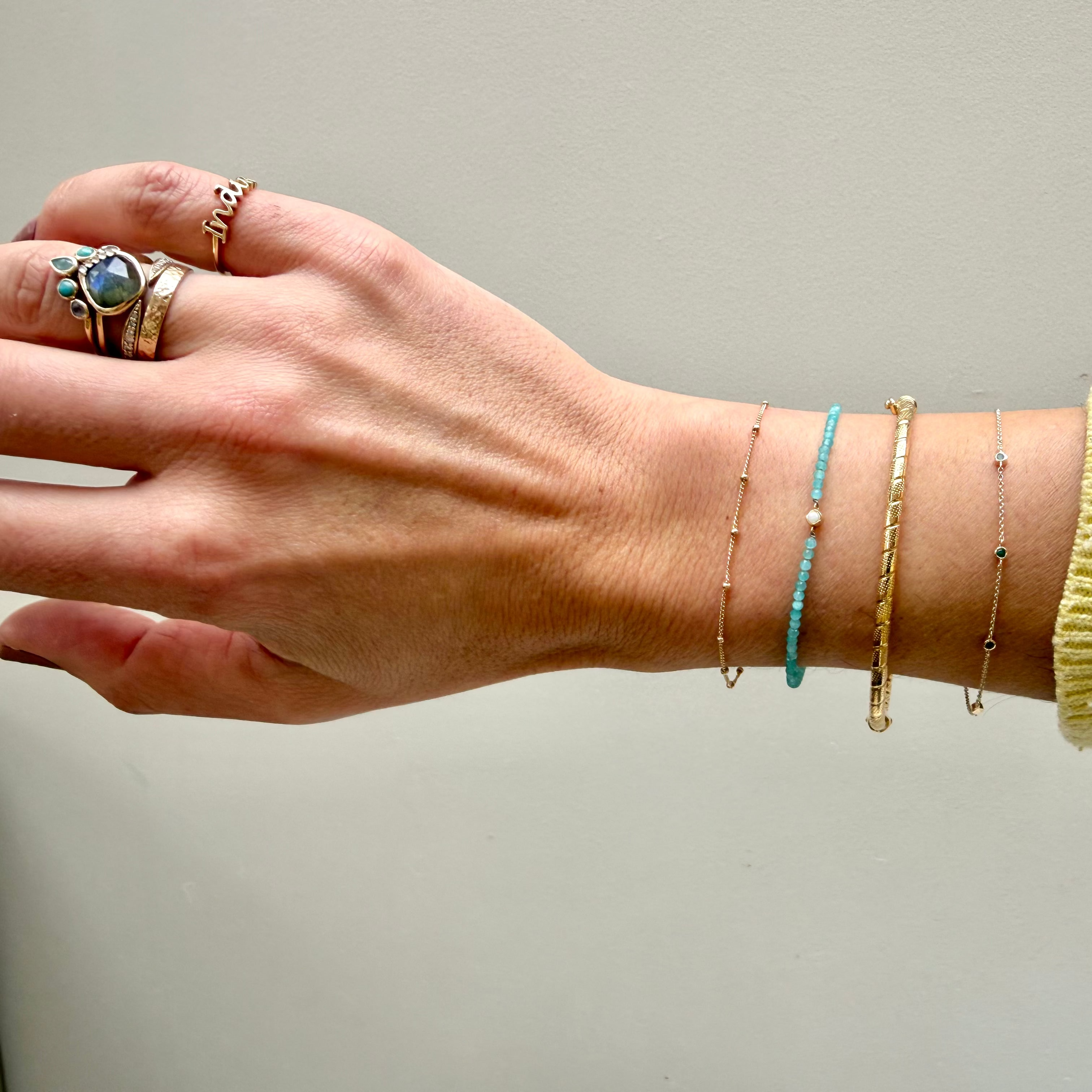 model hand wearing the Twisted Bangle 9k Gold along with other solid gold bracelets including the station bead bracelet and solid gold rings
