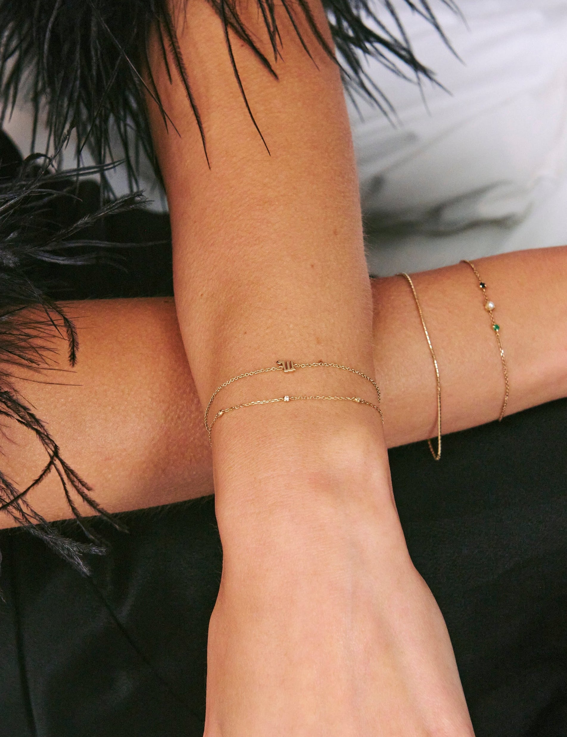 Close-up of a person's arm with gold bracelets and a ring, wearing a black feathered garment.