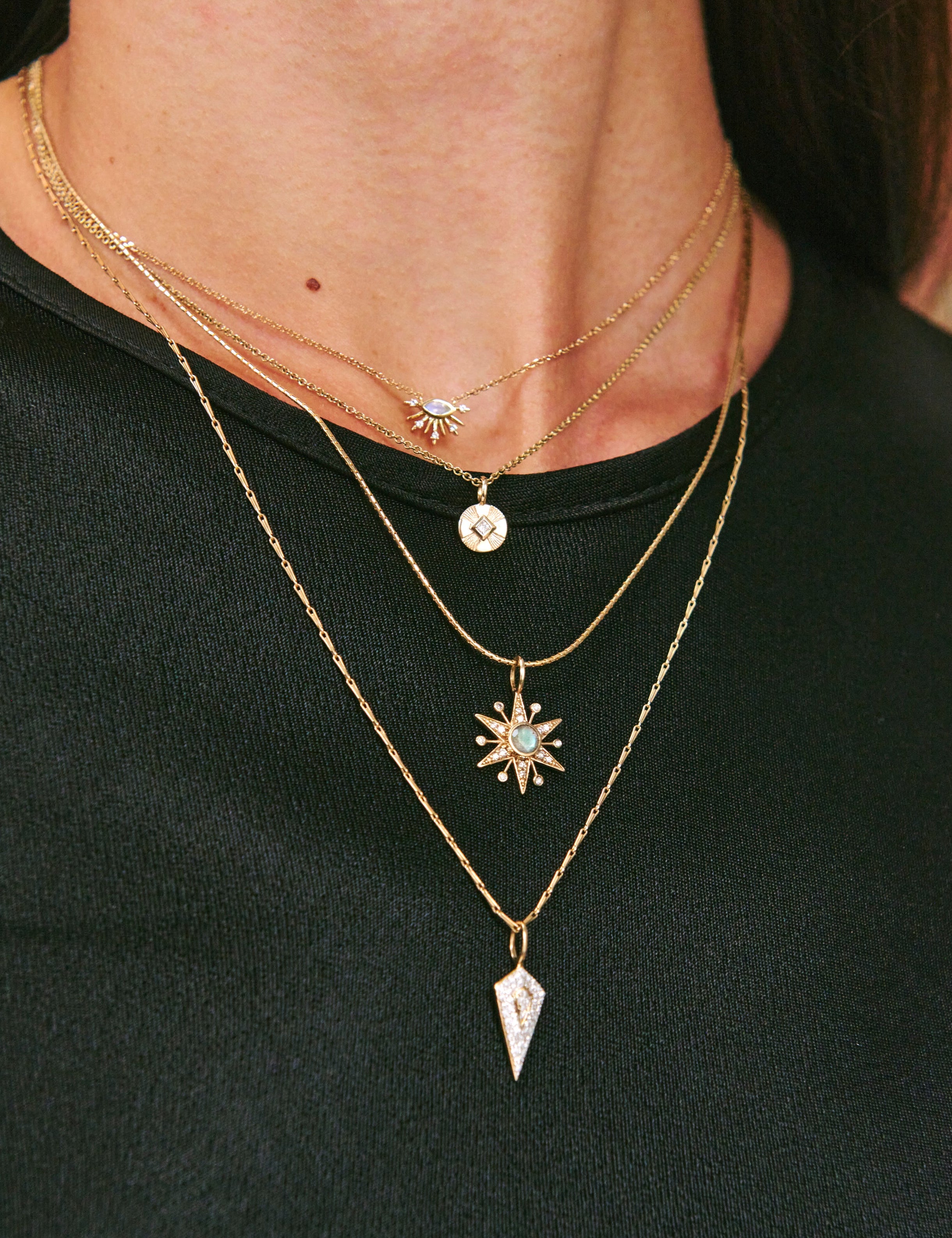 Layered gold necklaces with star and arrow pendants on a black background