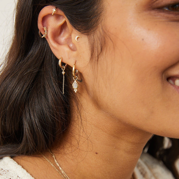 model wearing gold earring stack including the Diamond Starburst Huggie Hoop Earring 9k Gold with diamond charm earring