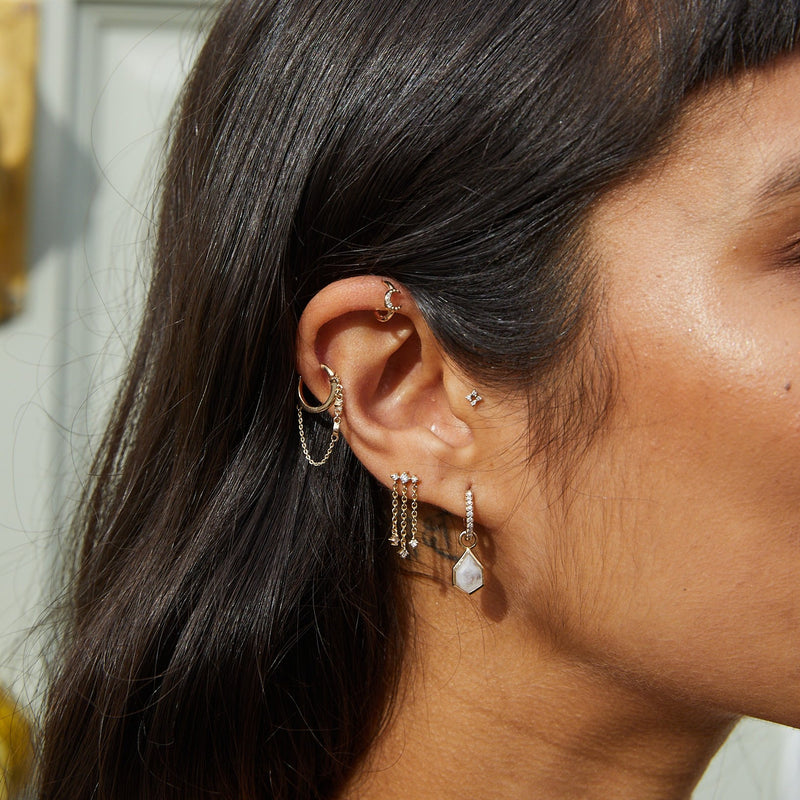 model wearing gold earring stack including the Diamond Moon Chain Huggie Hoop Earring 9k Gold on helix