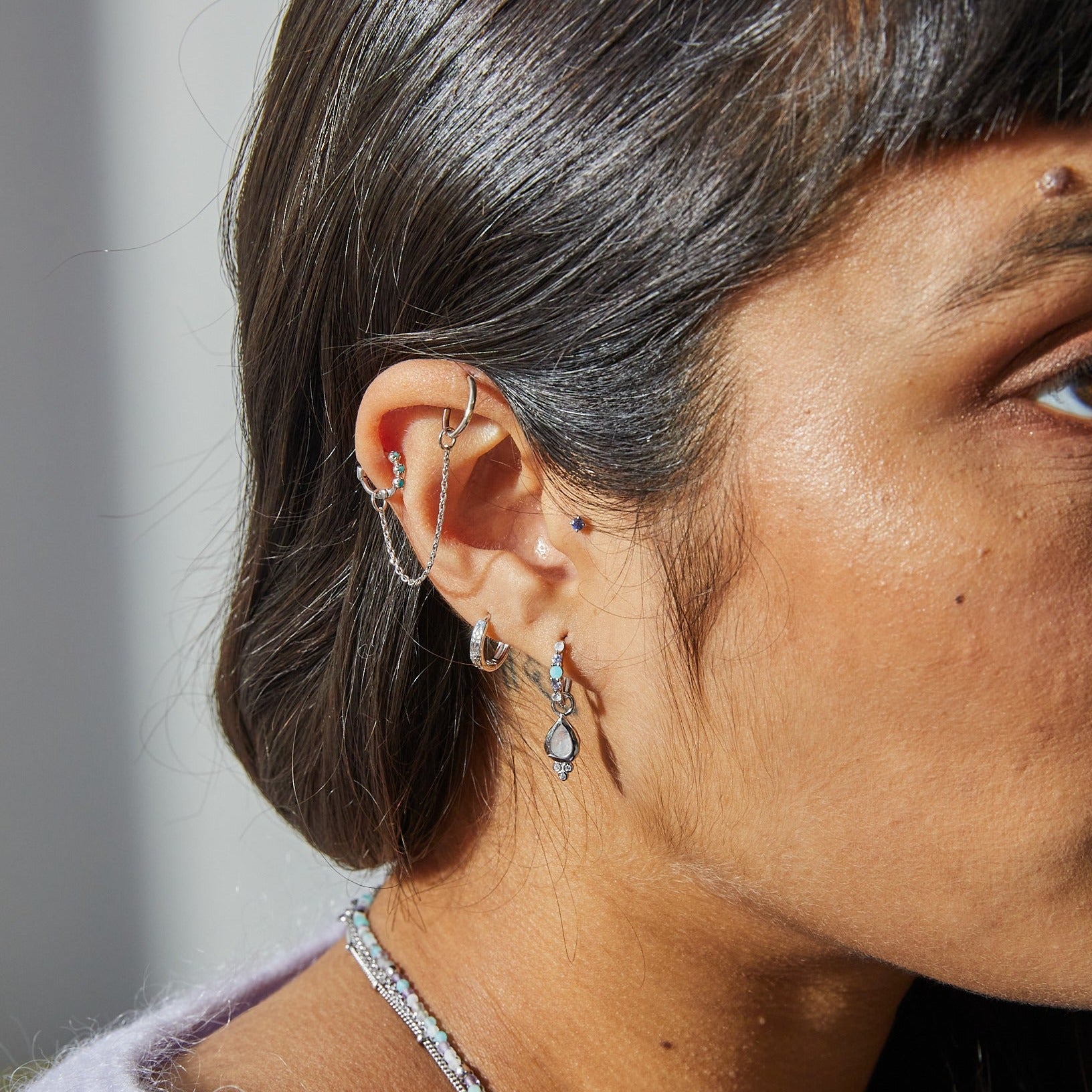 model wearing silver ear stack including the White Sapphire Starburst Huggie Hoop Earring Sterling Silver