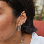 close up of the Medium Twisted Huggie Hoop Earring Sterling Silver on model ear with coin charm 