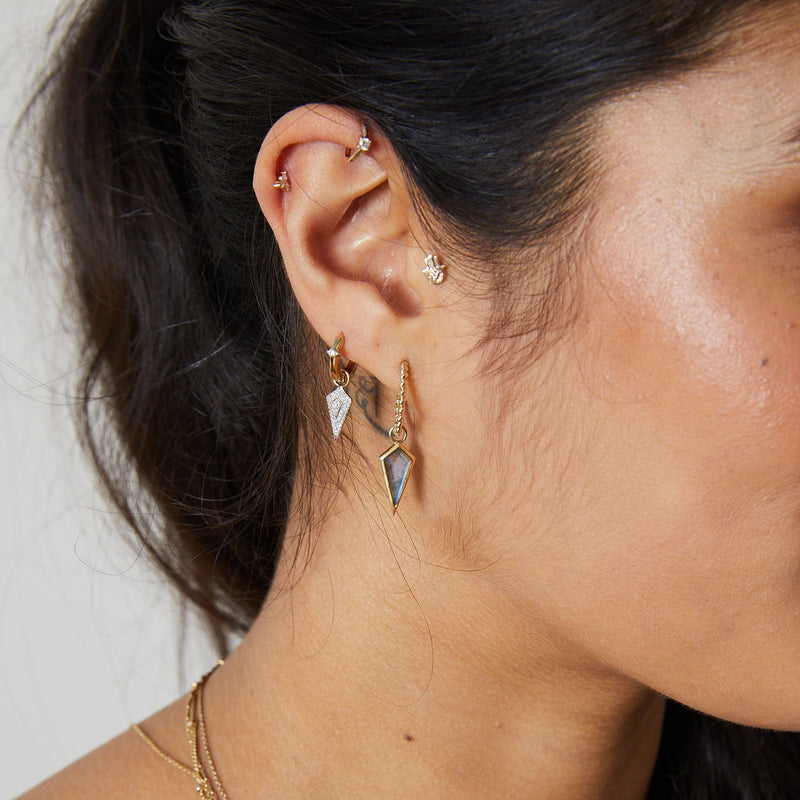 model ear wearing gold earring stack including the Medium Twisted Huggie Hoop Earring 9k Gold and labradorite rhombbus charm
