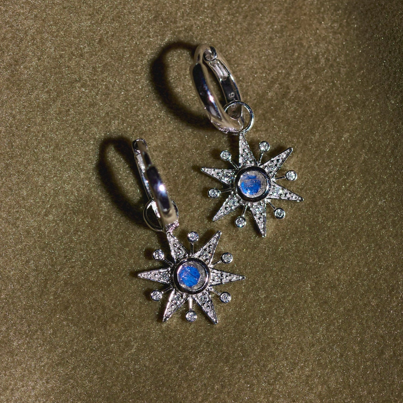 Pair of silver earrings with blue stones on a green fabric background