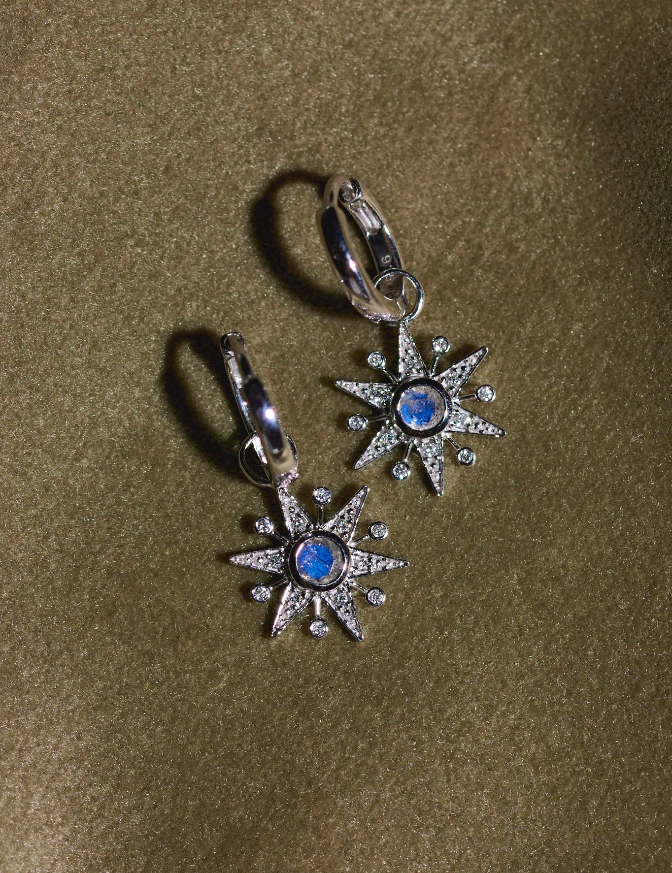 Pair of silver earrings with blue stones on a green fabric background