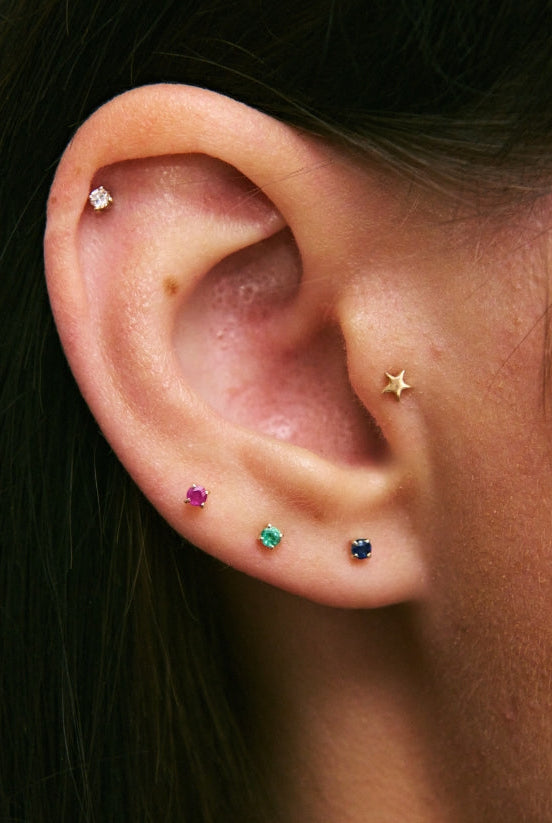 Close-up of an ear wearing multiple colorful earrings with a blurred background