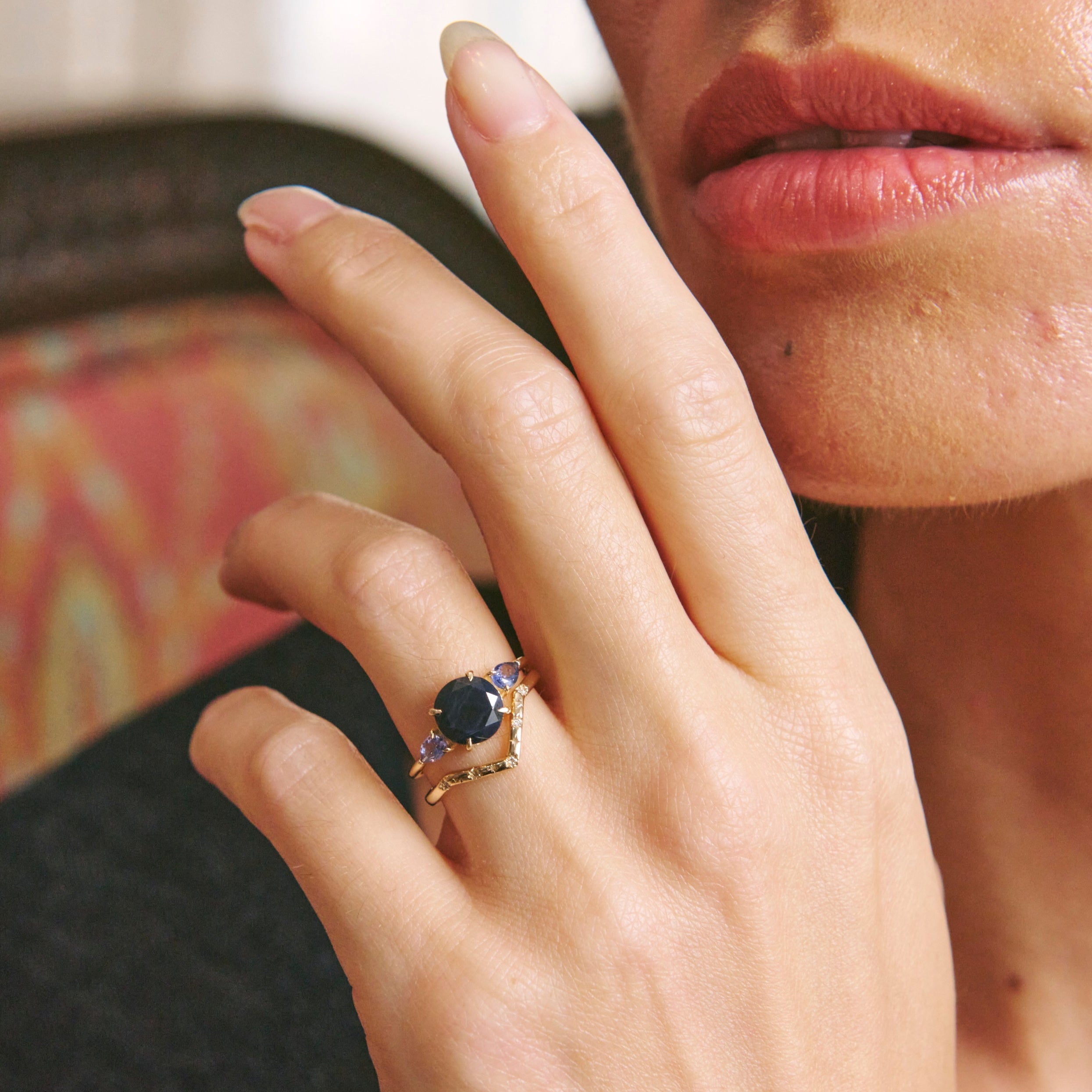 Close-up of a hand wearing a gold ring with a black gemstone, against a blurred background.