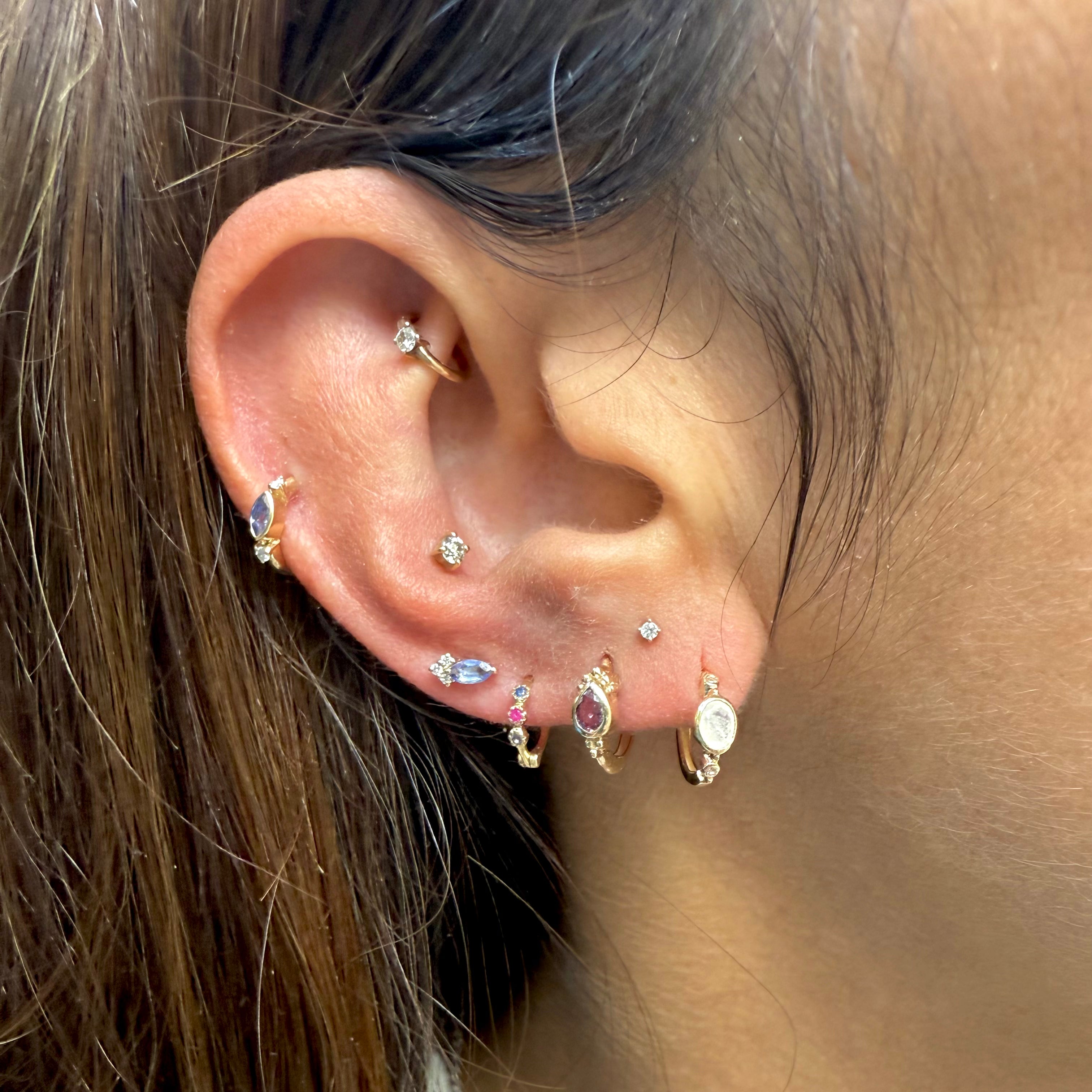 Close-up of an ear with multiple gold and gemstone earrings.