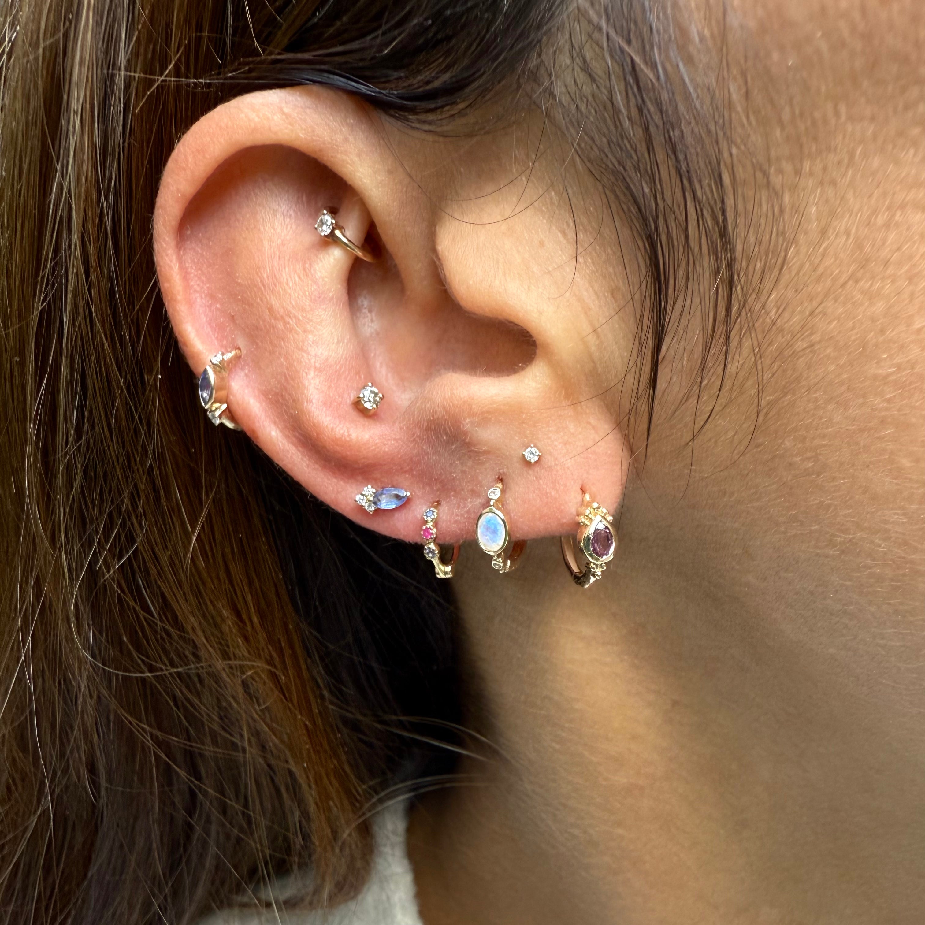 Close-up of an ear with multiple gold earrings featuring gemstones.