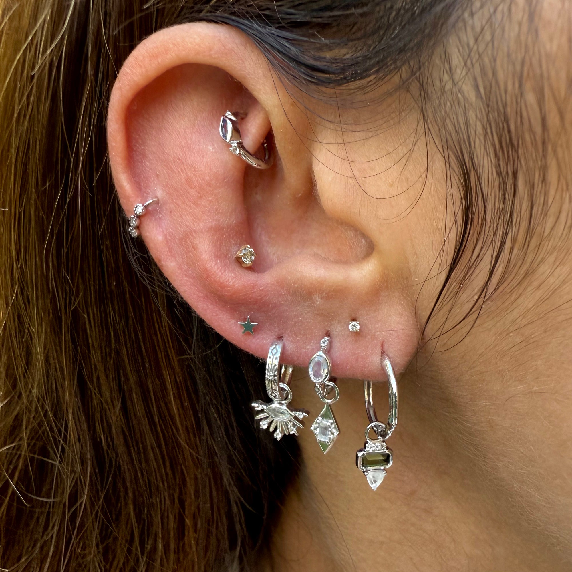 Close-up of an ear with multiple silver earrings and a nose ring.