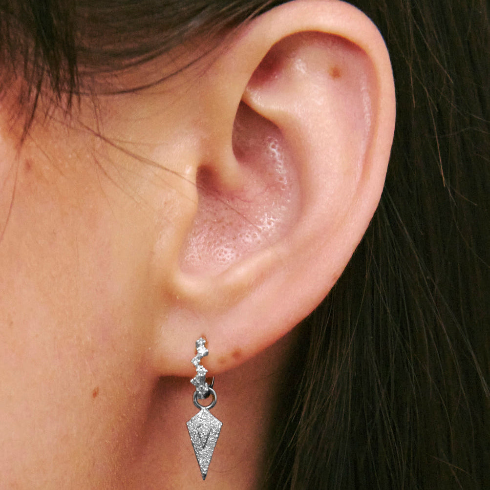 Close-up of an ear wearing a silver earring with a geometric design.