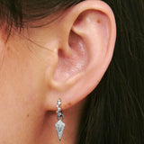Close-up of an ear wearing a silver earring with a geometric design.