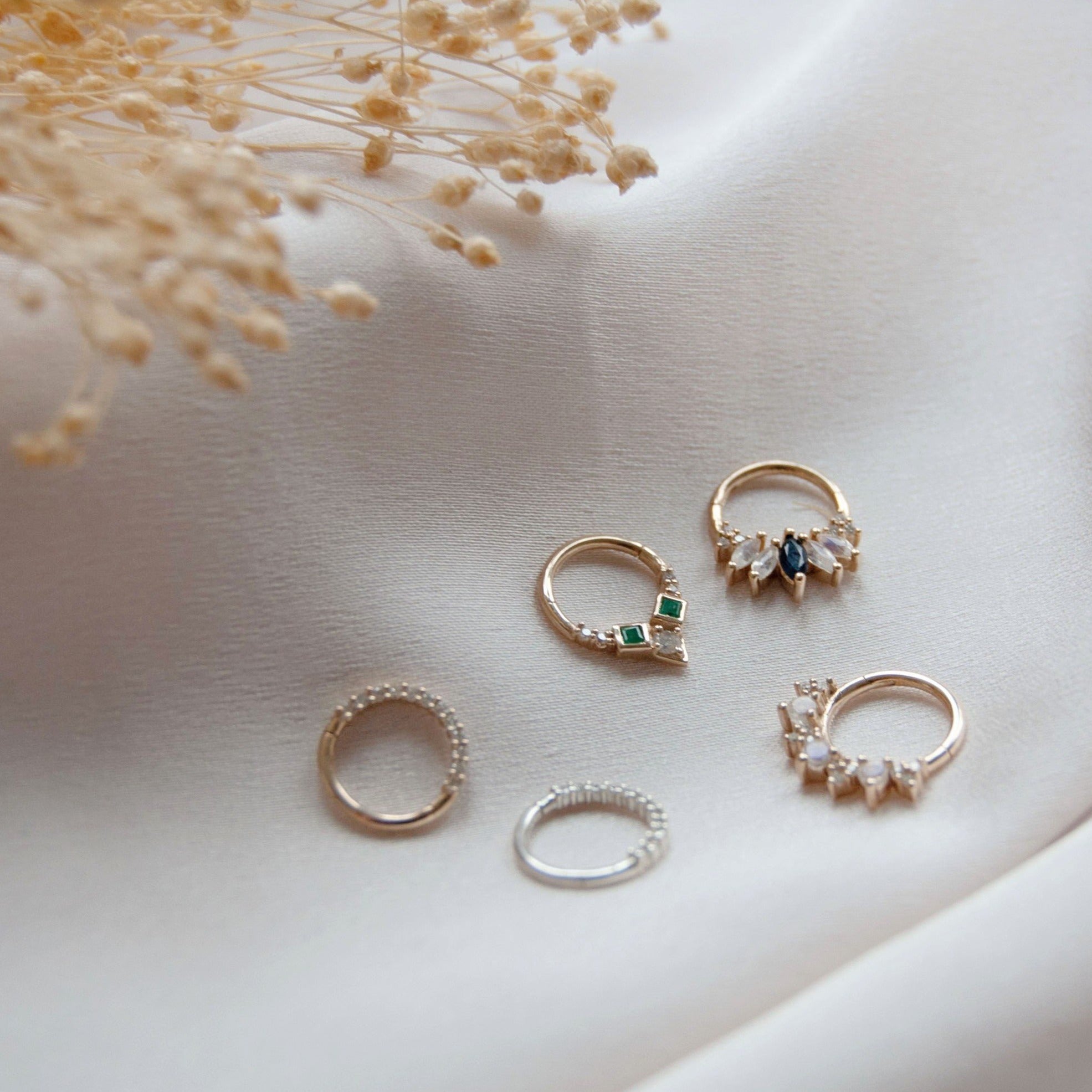 Display of 5 daith earring hoops on a white cotton display, with an individual emerald & diamond earring made with a 9 karat gold hoop focused on display 