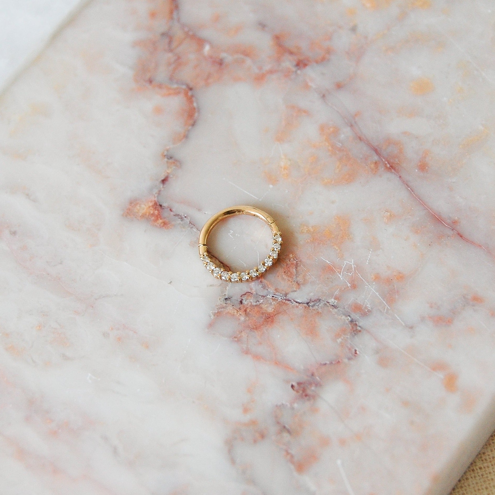 diamond pave hoop in 9k gold for daith piercings on a pink marble surface