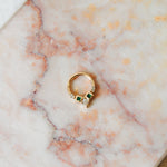 Emerald & diamond daith earring hoop made with 9 karat gold displayed on a pink marble background