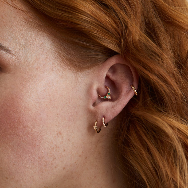 model wearing a daith earring stack with 9 karat gold hoops, featuring one emerald & diamond earring